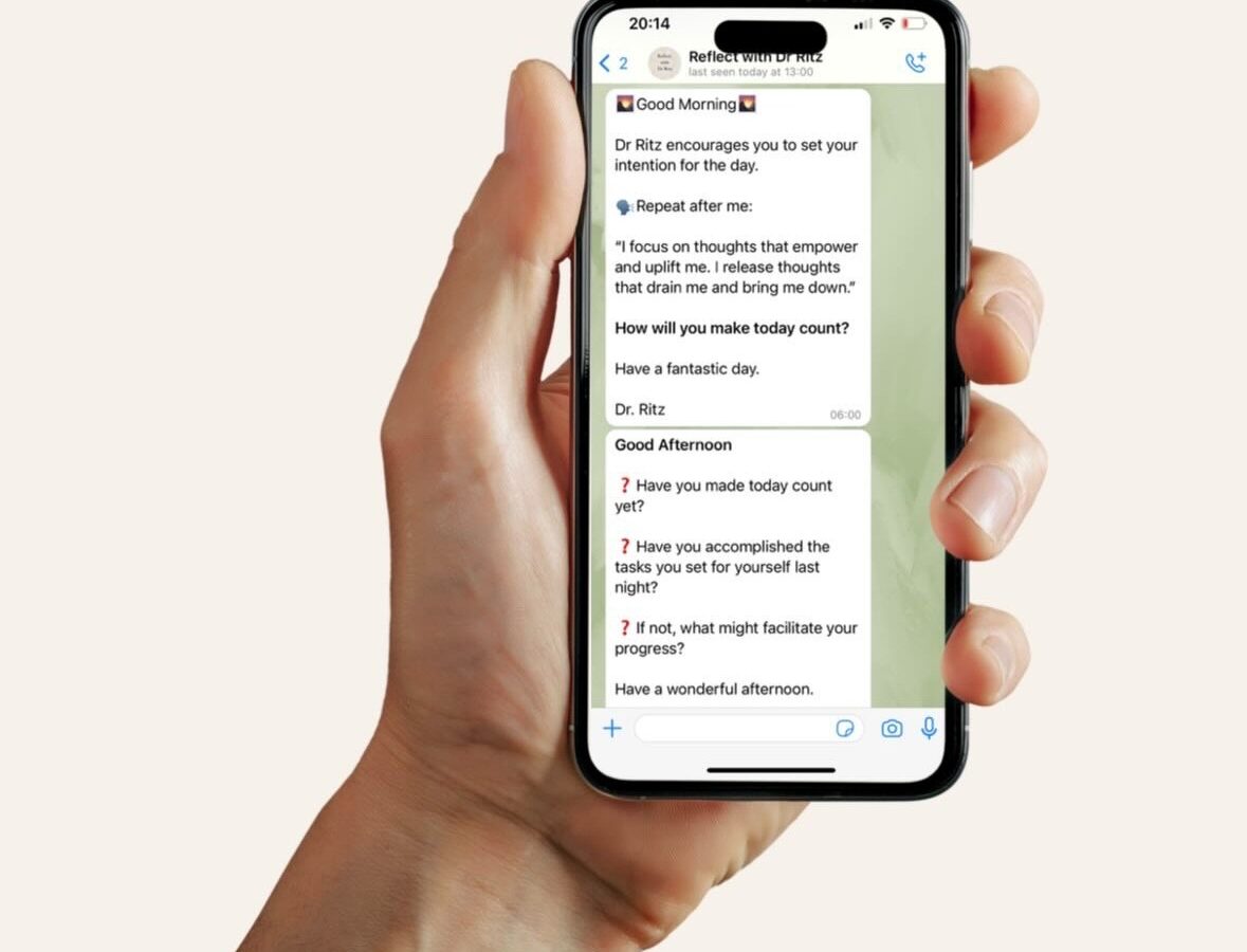 A hand holding a phone showing a Reflect with Dr. Ritz morning message on WhatsApp